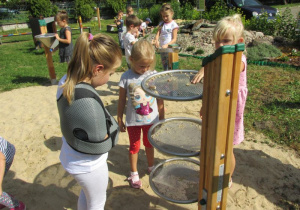 dziewczynki obserwują i doświadczają zachowania piasku na trzech sitach umieszczonych na drewnianym kołku jedno pod drugim